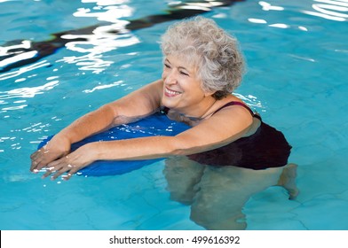 Happy senior woman with kickboard in a swimming pool. Old woman swimming in water with the help of a kickboard. Smiling old woman swimming with inflatable board in swimming pool.