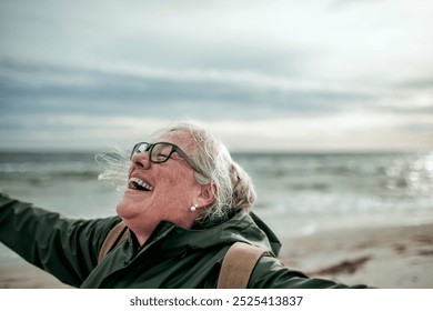 Happy senior woman laughing and enjoying the ocean breeze on a beach - Powered by Shutterstock