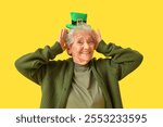 Happy senior woman with leprechaun hat on yellow background. St. Patrick