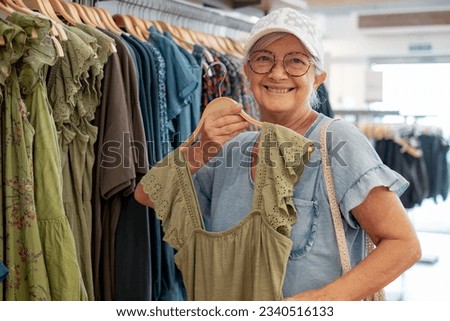 Happy senior woman looking for sale in a store selecting a green dresses enjoying shopping, consumerism sales customer shopping concept