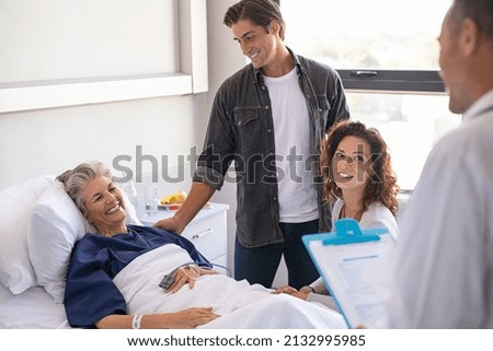 Happy senior woman lying on hospital bed with lovely son and daughter visiting and talking to doctor. Professional physician gives the results of the medical report to patient's family members.