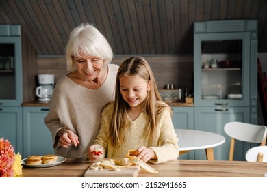 Happy Senior Woman Making Breakfast With Her Granddaughter In Kitchen At Home