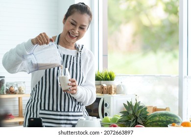 Happy senior woman making healthy smoothie drink for morning  at home kitchen, woman pours a smoothie  cocktail  from mixer into glass - Powered by Shutterstock