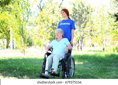 Happy Senior Woman On Wheelchair With Young Female Volunteer Outdoors