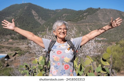 Happy senior woman with outstretched arms smiling enjoying the flowered natural park of almond trees in the spring time. Almond flowers blossoms.