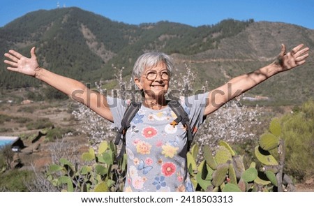 Happy senior woman with outstretched arms smiling enjoying the flowered natural park of almond trees in the spring time. Almond flowers blossoms.