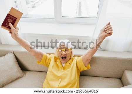 Happy senior woman with passport and travel ticket packed a red suitcase, vacation and health care. Smiling old woman joyfully sitting on the sofa before the trip raised her hands up in joy.
