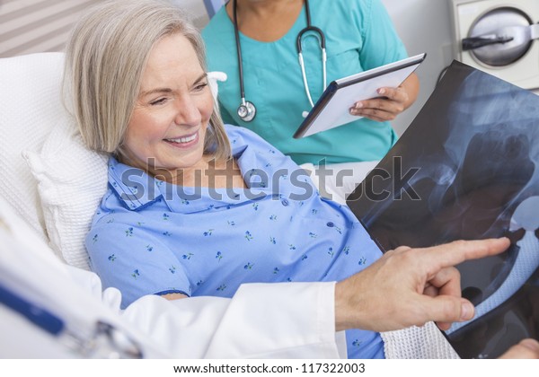 Happy\
senior woman patient recovering in hospital bed with male doctor\
and female nurse looking at hip replacement\
x-ray