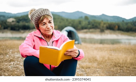 Happy senior woman reading a book outdoors during hiking day. Adventure and travel vacations concept - Powered by Shutterstock