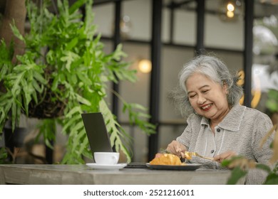 Happy Senior Woman Savoring Her Meal in a Green Cafe Setting. Enjoying Food, Nature, and Technology - Powered by Shutterstock