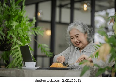 Happy Senior Woman Savoring Her Meal in a Green Cafe Setting. Enjoying Food, Nature, and Technology - Powered by Shutterstock