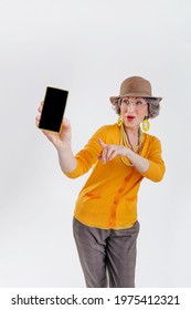 Happy Senior Woman Showing Empty Phone Screen Pointing To Phone On Light Grey Background With Blank Space For Text.