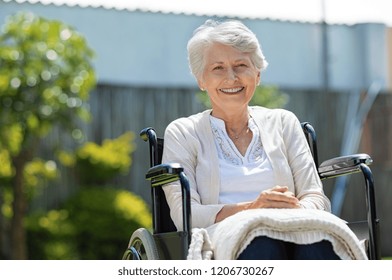 Happy senior woman sitting on wheelchair and recovering from illness. Handicapped mature woman sitting in wheelchair looking at camera. Portrait of a disabled elderly woman outdoor in a nursing home. - Powered by Shutterstock