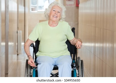 Happy Senior Woman Sitting In A Wheel Chair At Hospital Corridor