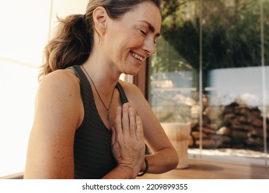 Happy Senior Woman Smiling While Meditating In Prayer Position At Home. Mature Woman Doing A Relaxation Exercise During A Yoga Session. Cheerful Elderly Woman Practicing A Healthy Workout Routine.