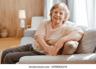 Happy senior woman smiling while relaxing. sitting on sofa at home looking at camera. Advertisement concept - Powered by Shutterstock