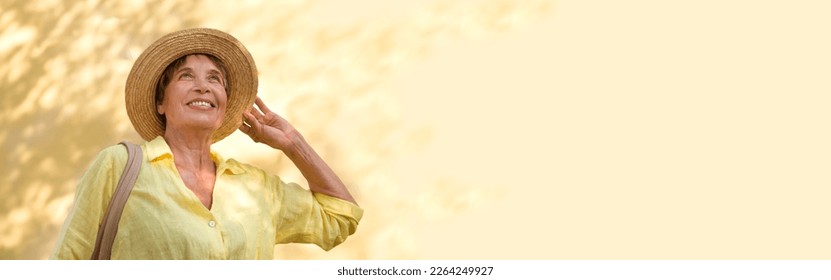 happy senior woman in sun hat walks  on summer city against the background of a yellow wall with shadows from trees. banner - Powered by Shutterstock