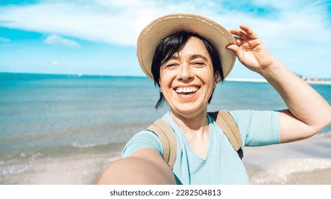 Happy senior woman taking selfie with smart mobile phone at the beach - Older female enjoying summer vacation - Summertime holidays, mature people and traveling concept - Powered by Shutterstock