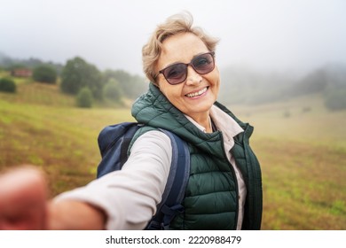 Happy senior woman traveler with backpack taking selfie during trekking trip in forest - Powered by Shutterstock
