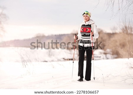 Happy senior woman walks with nordic walking sticks on white background of snow and nature. Sports active winter lifestyle