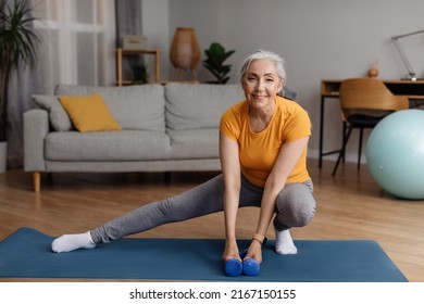 Happy senior woman warming up, doing legs stretching exercises while working out at home on fitness mat, looking and smiling at camera - Powered by Shutterstock