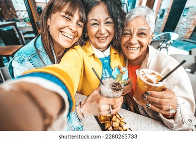 Happy senior women drinking cocktail glasses sitting at bar table - Group of best friends enjoying happy hour cheering drinks at pub restaurant - Life style concept with girls hanging out together - Powered by Shutterstock