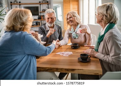 Happy senior women handshaking after playing cards with their friends at home. 