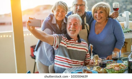 Happy Seniors Friends Taking A Selfie Photo With Smartphone Camera At Barbecue Dinner In House Terrace - Mature People Having Fun With New Trend Technology - Focus On Mobile Cell Phone 