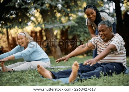 Happy seniors stretching while having exercise class with physiotherapist in backyard of residential care home. Focus is on African American man.