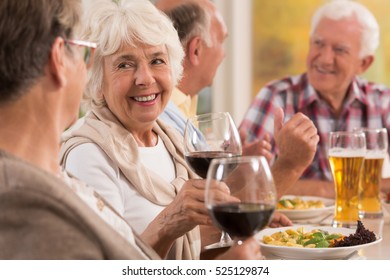 Happy Seniors Talking And Smiling During Dinner, Drinking Beer And Wine