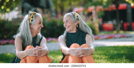 Happy Seniors Women, Twins Sitting In City Park, Smiling And Talking.