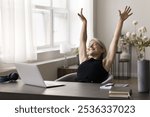 Happy serene mid aged lady office worker stretch hands up enjoy friday end of workday after job is done. Smiling senior woman freelancer relax rest do simple gymnastics at workplace in moment of peace