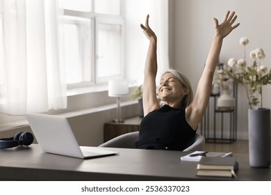 Happy serene mid aged lady office worker stretch hands up enjoy friday end of workday after job is done. Smiling senior woman freelancer relax rest do simple gymnastics at workplace in moment of peace - Powered by Shutterstock