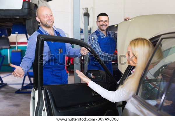 Happy service crew and woman driver standing near\
car and smiling. Focus on\
man