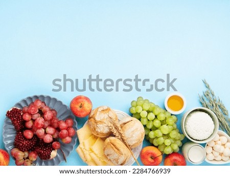 Happy Shavuot festive card. Jewish religious holiday concept. Dairy products, grapes, cheese, bread, milk, cottage cheese, wheat, honey on blue background. Top view, copy space.