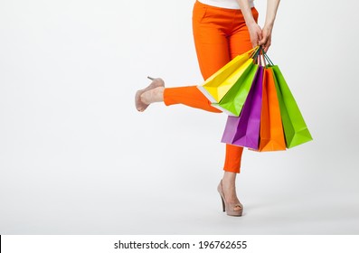 Happy shopping! Unrecognizable woman in orange pants holding multicolored shopping bags