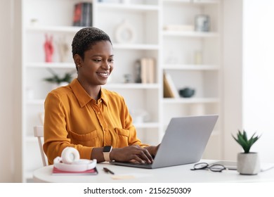 Happy short-haired millennial african american lady freelancer using laptop at home, sitting at workdesk with wireless headset on, smiling, copy space. Remote job, digital marketing concept - Powered by Shutterstock