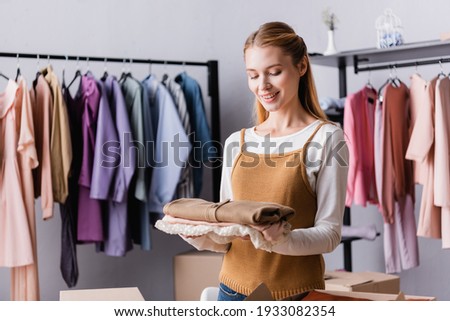 happy showroom proprietor holding clothes near hangers on blurred background