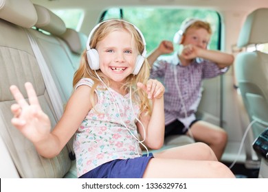 Happy siblings. Children listen to music on headphones in the car and sing to it - Powered by Shutterstock