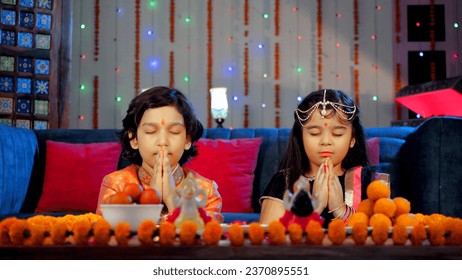 Happy siblings in an ethnic dress doing a religious Diwali Puja together. A table decorated with marigold flowers and traditional Indian sweets - a Hindu festival, religious ceremony, festive seaso...