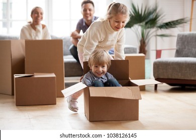 Happy siblings having fun moving into new home, smiling sister helping excited little boy riding in cardboard box, cute kids playing together in living room, family with children relocating concept - Powered by Shutterstock