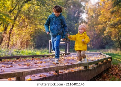 Happy siblings running on wood path walk in sunny autumn forest, playing catch-up game