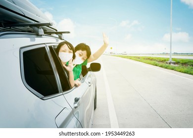 Happy Siblings Wearing Face Mask While Waving Hands During Travel By Car With Blue Sky Background. Summer Road Trip Concept