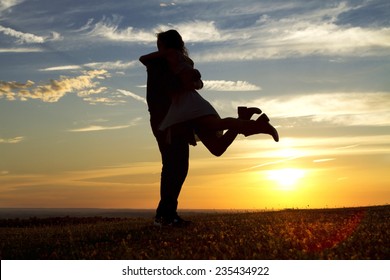 Happy silhouette couple embracing as the answer is yes to a marriage proposal against the background of sunset