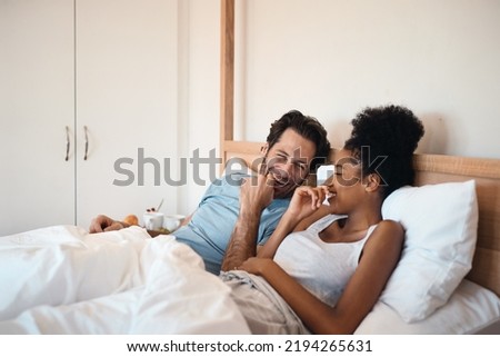 Happy, silly and goofy couple bonding in bed, sharing intimate relationship joke and moment. Young interracial husband and wife laughing, loving and enjoying lazy morning relaxing indoors together