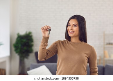 Happy Single Beautiful Young Woman Showing Keys To Her New Home, Looking At Camera And Smiling. Portrait Of Proud First Time Buyer, House Owner Or Apartment Tenant. Buying Your Own Property Concept