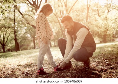 Happy single father tying his daughter shoes in park. - Powered by Shutterstock