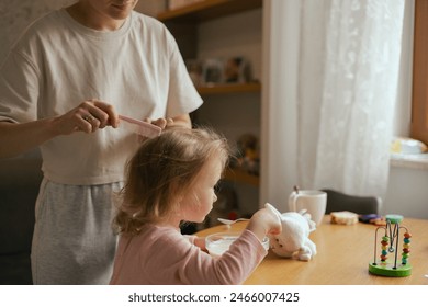 Happy single mother doing her daughter's hair while having breakfast. Woman combs the hair of a little girl. The concept of morning routine, single parenthood and preparation for school. - Powered by Shutterstock