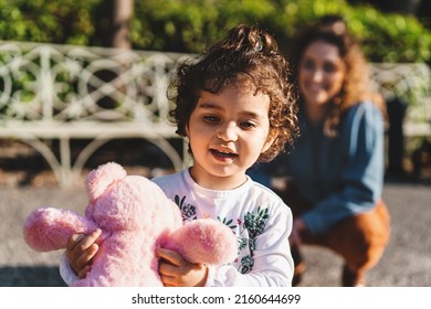 Happy Single Mother And Doughter Playing And Running Outdoors In The Park- Child Holding A Teddy Bear And Mom Blurred In Background, Life Style Family Concept
