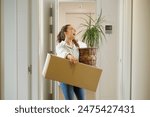 Happy Single pretty young adult woman arriving entering the door of her new moving house with boxes and a plant, real estate, house selling